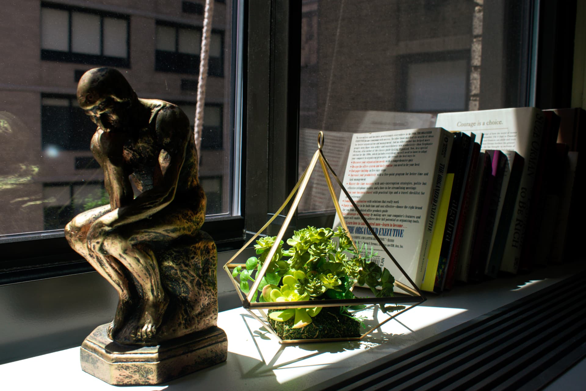 Sunlit office windowsill with The Thinker sculpture, plant, and books